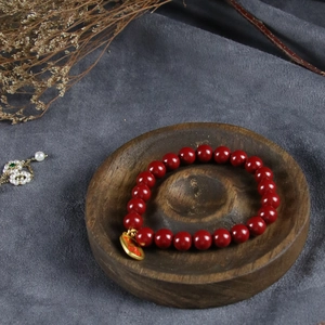 Deep red beaded bracelet with golden Fu pendant displayed on a solid wood tray