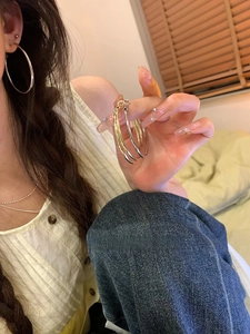 Detail view of large gold and silver minimalist hoop earrings held against a warm room