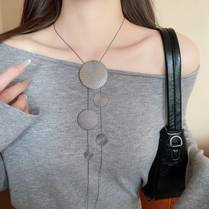 Detail of a silver geometric tassel necklace on a model wearing a grey sweater