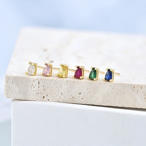 Macro shot of colorful pear-cut zircon earrings set in gold on a beige stone surface