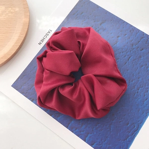 Detail of dark red satin scrunchie with soft pleats on a stylish magazine background