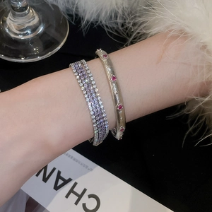 Nahaufnahme von mehrlagigen Zirkonia-Armbändern und gebürstetem Metallreif mit roten Steinen