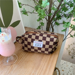 Détail d'une trousse à maquillage en velours côtelé à damier marron sur table en bois