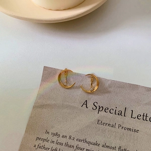 Vue macro de boucles d'oreilles lune dorées avec zircon sur une carte texte esthétique