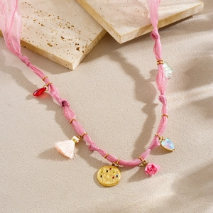Pink ribbon necklace detail featuring gold charms, floral motifs and a white tassel