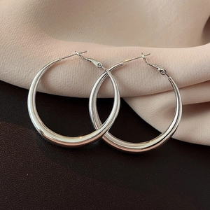Close-up of silver-tone large hoop earrings with polished finish on satin and leather background