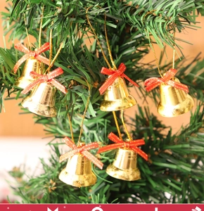 Close-up of golden Christmas bells with red bows hanging on an evergreen pine branch