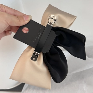 Handheld view of a dual-color satin bow hair clip with a sturdy metal alligator base