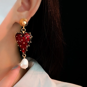 Close-up of vintage gold-plated heart earrings with red enamel and pearl drop on model