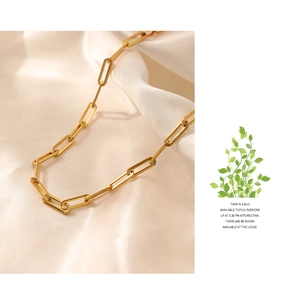 Golden paperclip chain necklace on beige silk fabric with soft elegant lighting