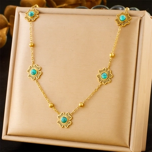 Close-up of gold chain necklace with five turquoise flower pendants on beige pad