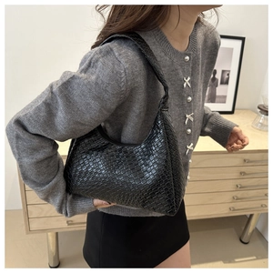 Side view of black woven shoulder bag worn by model in minimalist interior setting