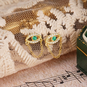 Detailed view of evil eye stud earring with green gemstone and gold chain tassel