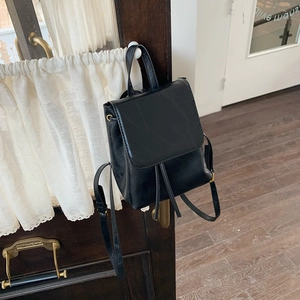 Dettaglio di un piccolo zaino vintage nero appeso a una porta in legno con pizzo