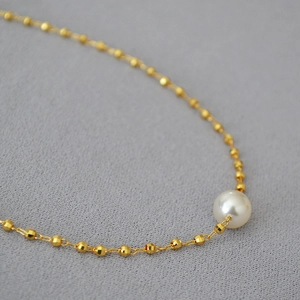 Macro shot of white round pearl on laser-cut gold-plated brass bead chain necklace