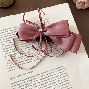 Detailed close-up of pink satin bow hair clip with zircon embellishment and red ribbon