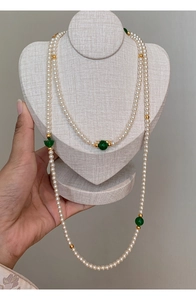 Detail of long artificial pearl necklace with green accent beads on neck display