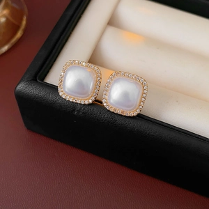 Detail of square gold earrings with large white pearl centers and zircon stone accents