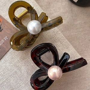 Detail view of resin cross claw clips with large white pearls and a classic tortoiseshell finish