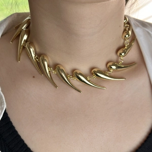 Close-up of golden spiky thorn necklace showing detailed curved metallic charms on neck