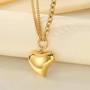 Detail of gold layered necklace with hollow heart pendant on textured beige fabric