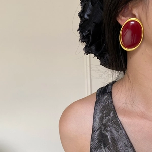 Close-up of red oval earring with gold trim worn by a model in silver sequin top