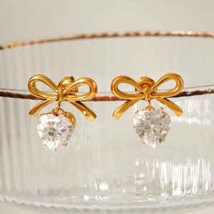 Golden bow-knot stud earrings with hanging heart zircon crystals shown on glass edge
