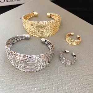 Detail of layered wavy metal bracelets and rings with textured finish in gold and silver
