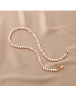 Freshwater pearl necklace with golden OT clasp over a beige silk texture background