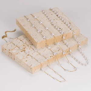 Elegant gold pearl necklaces with heart charms and oval accents on travertine stone base