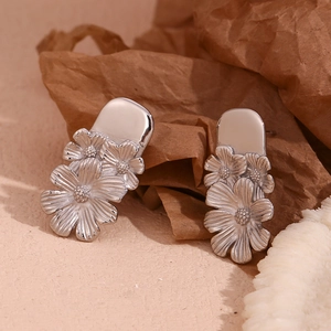 Macro view of silver floral daisy stud earrings on vintage paper and coral background