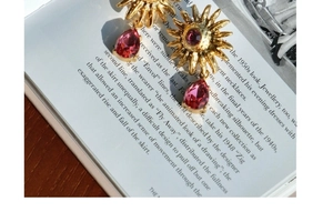 Detail shot of vintage gold sunflower earrings with pink gems and a purple drop pendant
