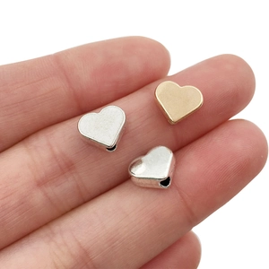 Macro shot of 8mm heart-shaped gold and silver beads on a finger for size reference