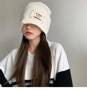 Close-up of white knitted beanie featuring a minimalist woven patch design and soft texture