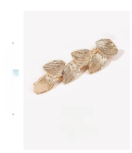 Detalle del pasador de pelo de metal dorado con textura cepillada y diseño de hojas