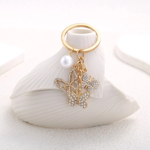 Elegant gold butterfly keychain with pearls and crystals on white shell vase