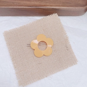 Close-up of a yellow acrylic flower hair clip on rustic linen and white textured background