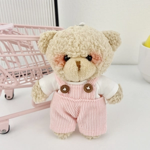 Dettaglio dell'orsetto di peluche bianco con salopette rosa e mini carrello della spesa