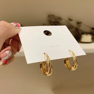 Chic double-layered gold geometric hoop earrings held against a blurred warm background