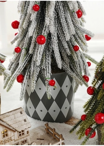Macro detail of snow-covered mini Christmas tree with red berries in a diamond-patterned pot