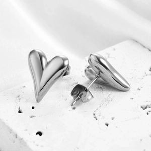 Macro shot of silver heart stud earrings on white stone and velvet background