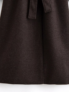 Close-up of thick dark wool coat fabric showing high-quality stitching and belted detail