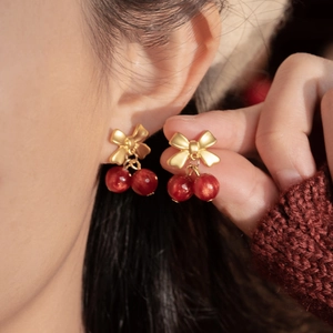 Detail of red cherry bow earrings on a model with a cozy burgundy winter sweater