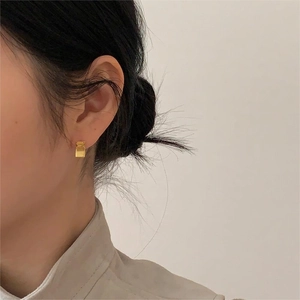 Close-up of golden geometric rectangle earrings on model showing brushed metal texture
