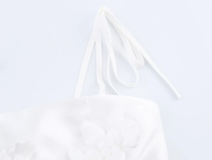 Detail of delicate white spaghetti strap top featuring a handcrafted 3D floral appliqué