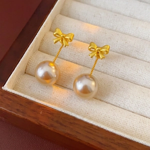 Elegant gold bow earrings with champagne pearls displayed on a premium jewelry tray