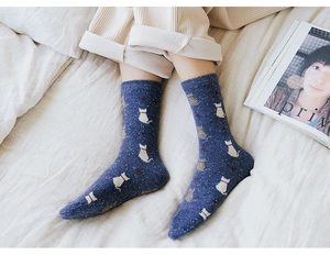 Detail of navy blue wool knit socks with cute white cat patterns in a cozy home setting