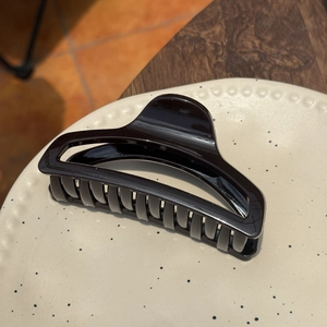 Close-up of a large glossy black perfume bottle shaped hair claw clip on a ceramic tray
