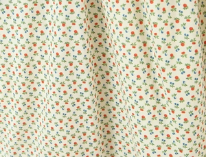Detailopname van bloemenprint op ivoren jurk met rode en blauwe bessenpatronen
