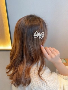 Detail of a pearl bow hair clip worn on long brown hair for a stylish side hairstyle